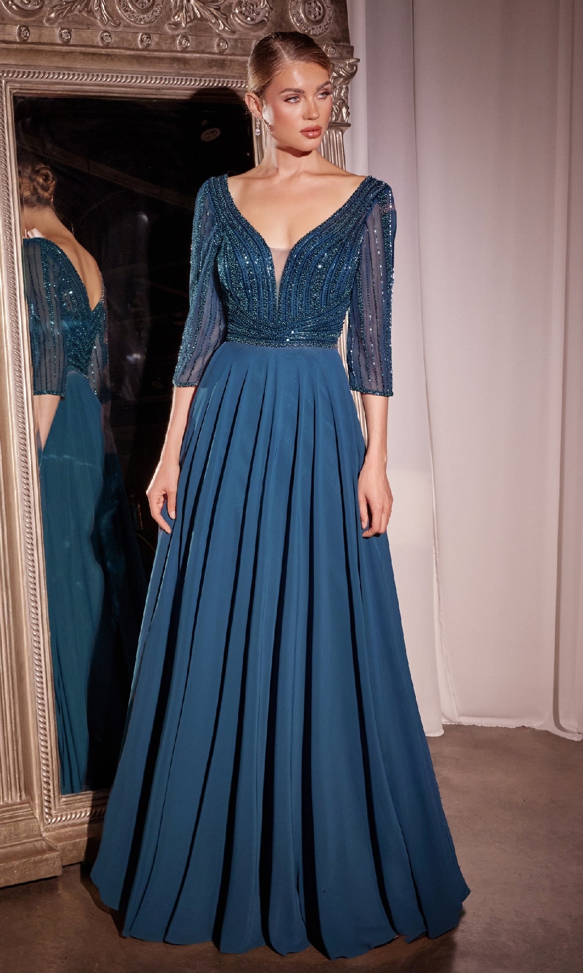 A woman stands before a mirror in the Modest Long A-Line Formal Dress: Ladivine CC446, featuring a beaded bodice, sheer three-quarter sleeves, and a pleated skirt—ideal as a mother of the bride dress.